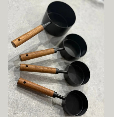 Set of black measuring cups with wooden handles on a gray surface